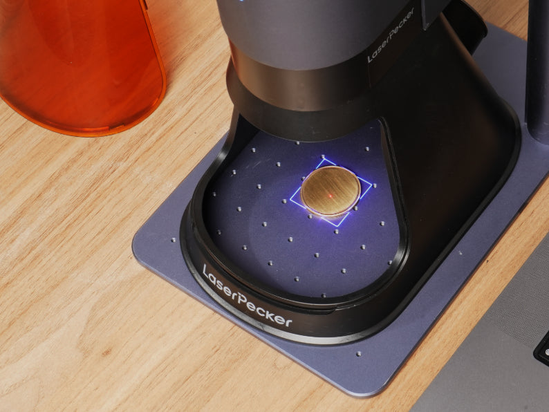 LaserPecker LP5 Laser Unit in preview mode, projecting a blue alignment beam onto a metal coin blank on the LaserPecker mat, demonstrating the real-time preview function of the engraving process.