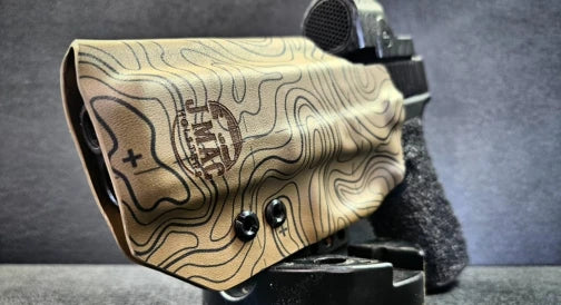 A customized leather holster engraved with a topographic pattern and logo attached to a tactical accessory.